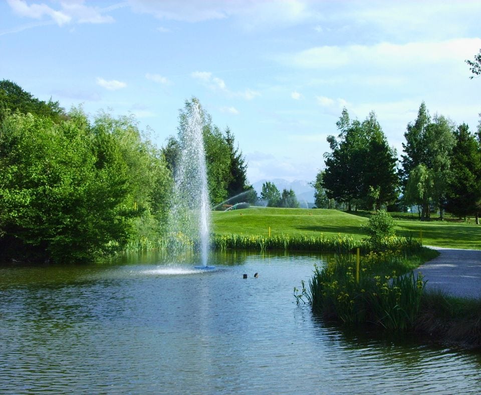 Fontäne im Teich auf einer Golfanlage neben einem Weg.